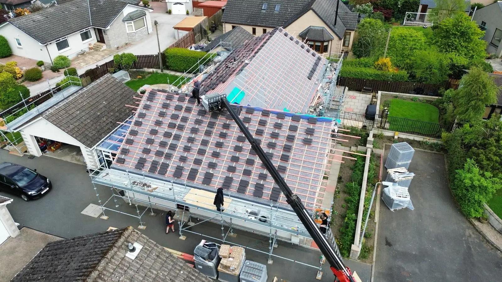 A crane lifting new tiles onto the bungalow roof