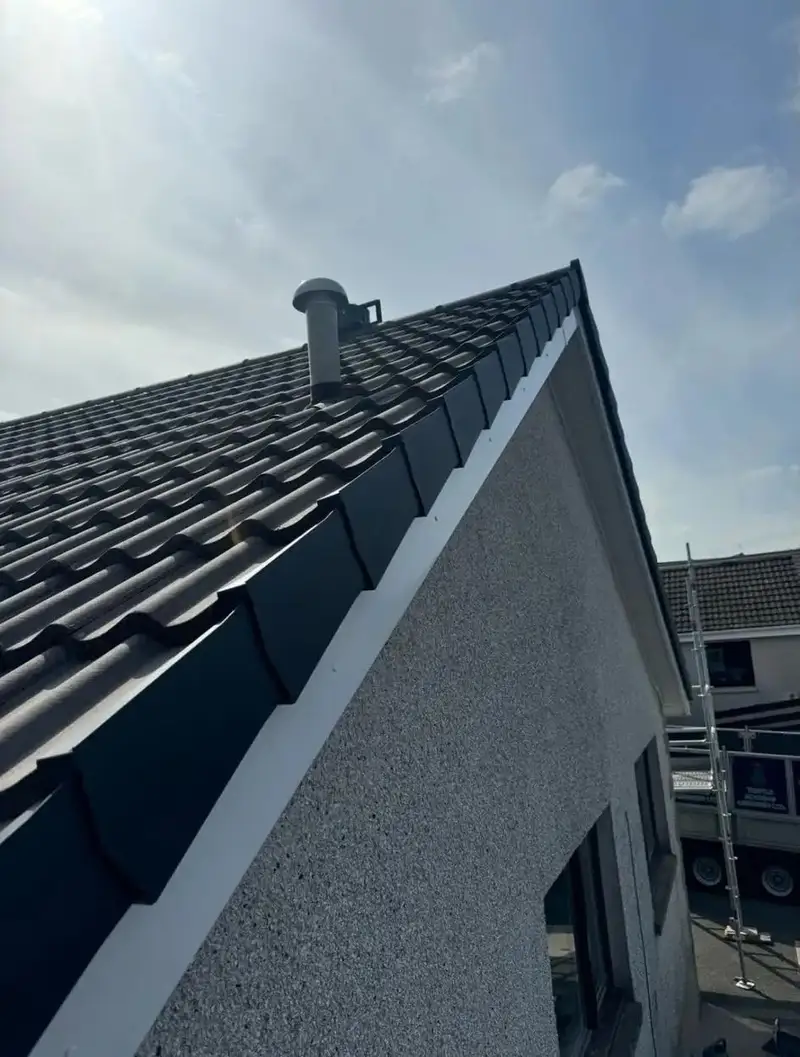 Gable end of a re-tiled roof finished with black dry-verge caps above a white bargeboard