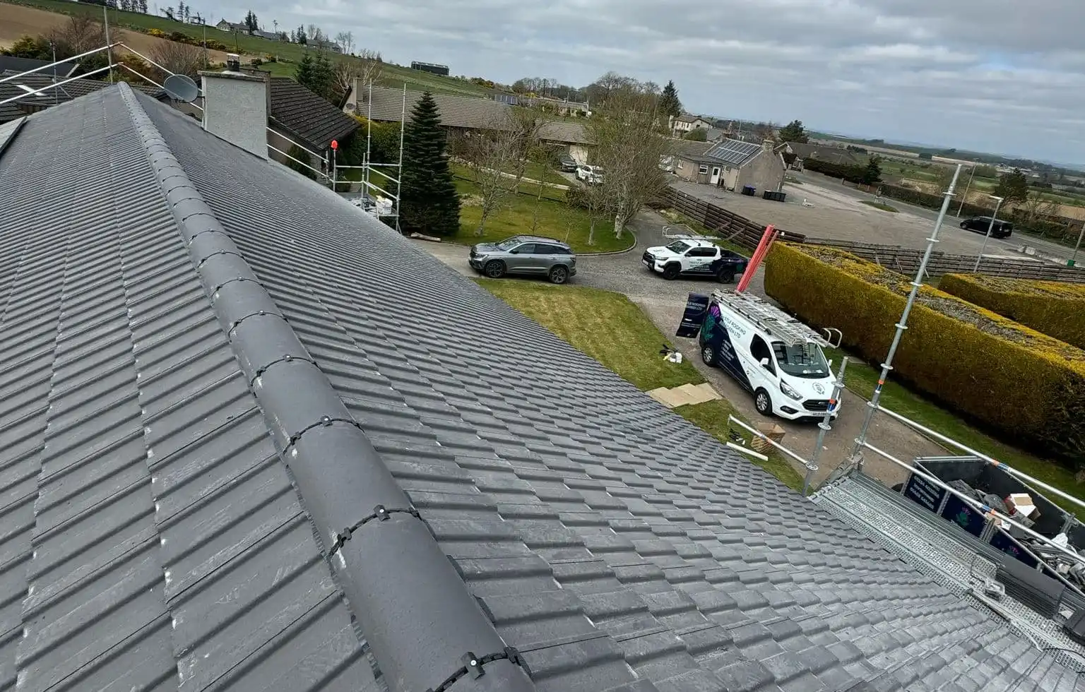 A finished re-tile in grey concrete tiles, seen from the ridge, with the Thistle Roofing van parked below