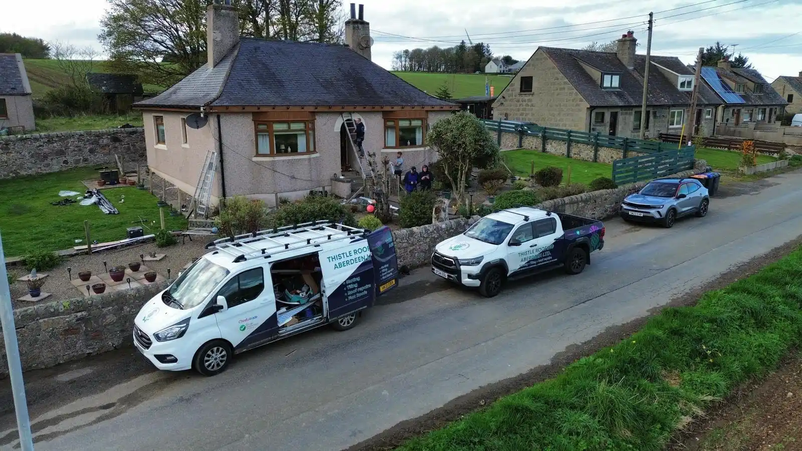 Two Thistle Roofing vans parked outside a bungalow while the team works on the roof