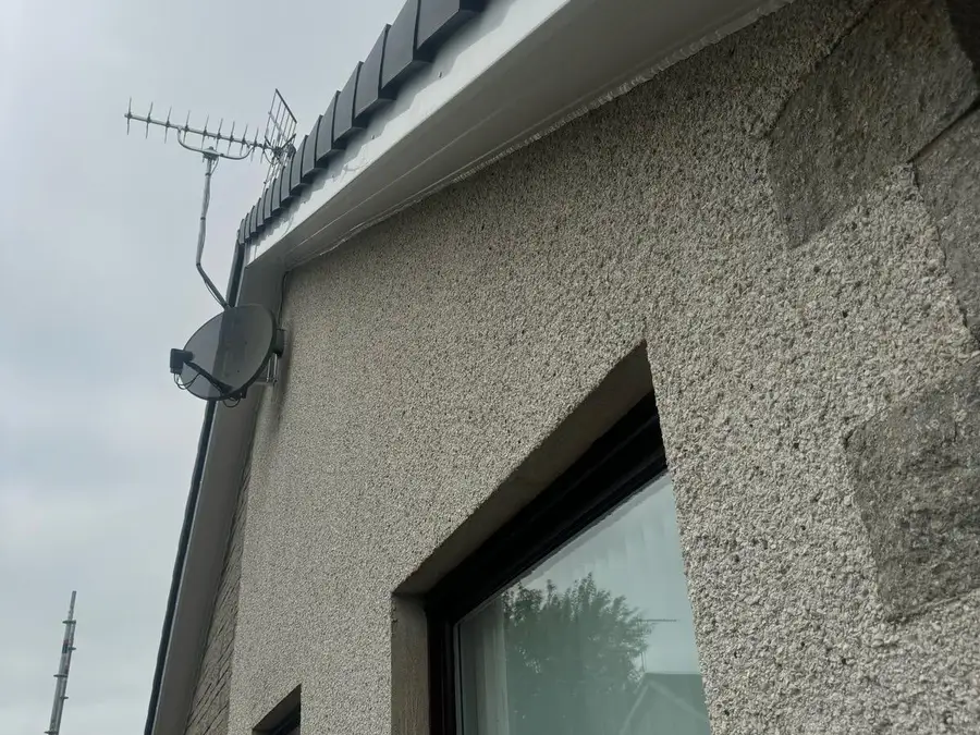 New white fascia and guttering along the eaves of a roughcast house