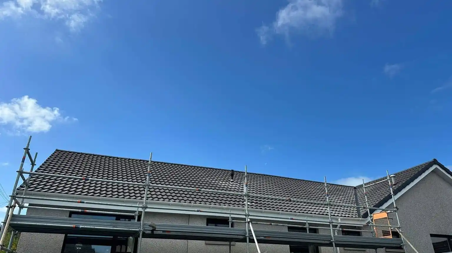 Scaffold along a house with a newly tiled roof and a new white roofline
