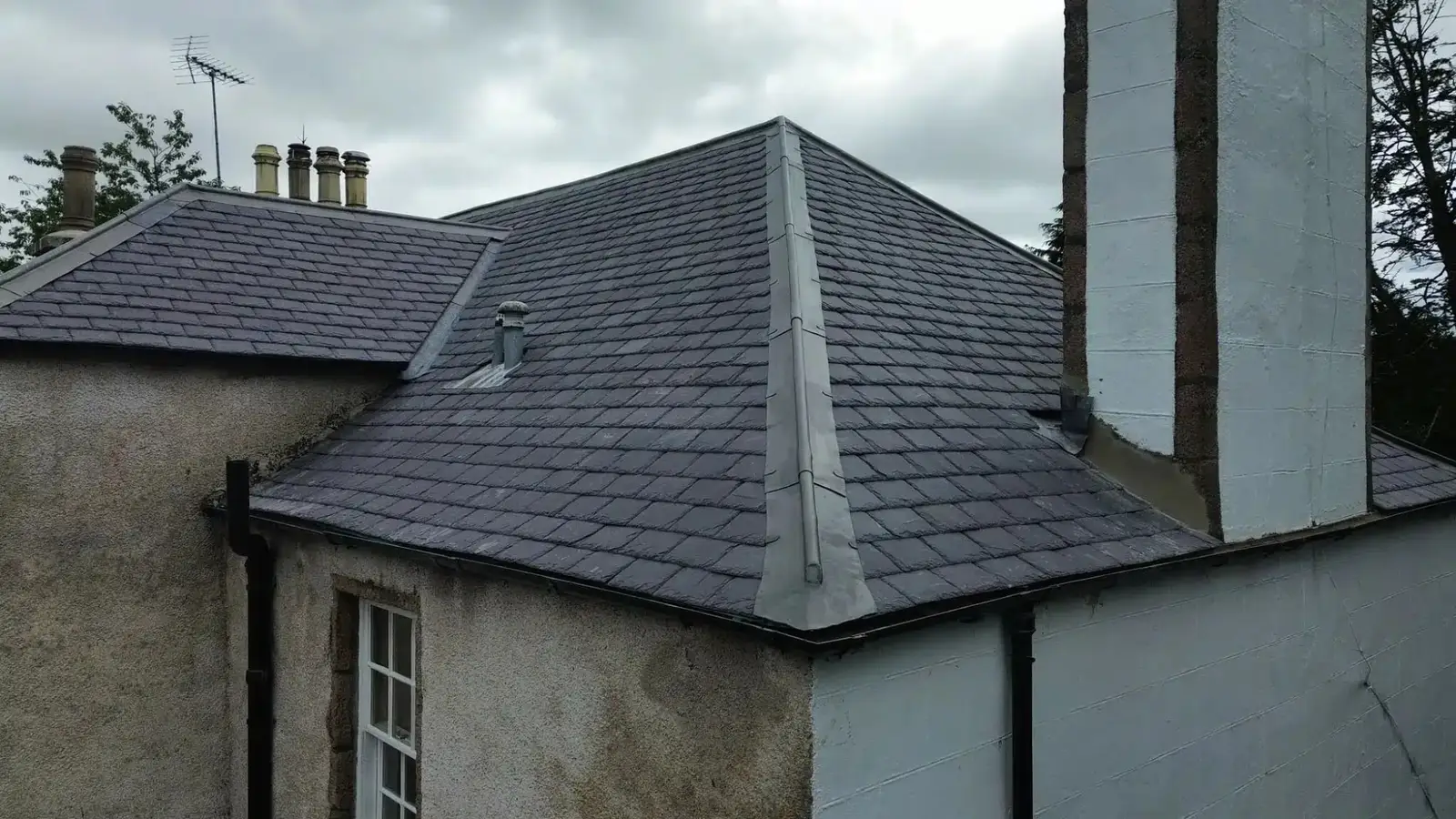 A hipped slate roof beside a tall white chimney stack