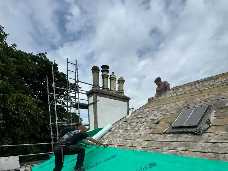 A roofer laying green breathable membrane on a slate roof