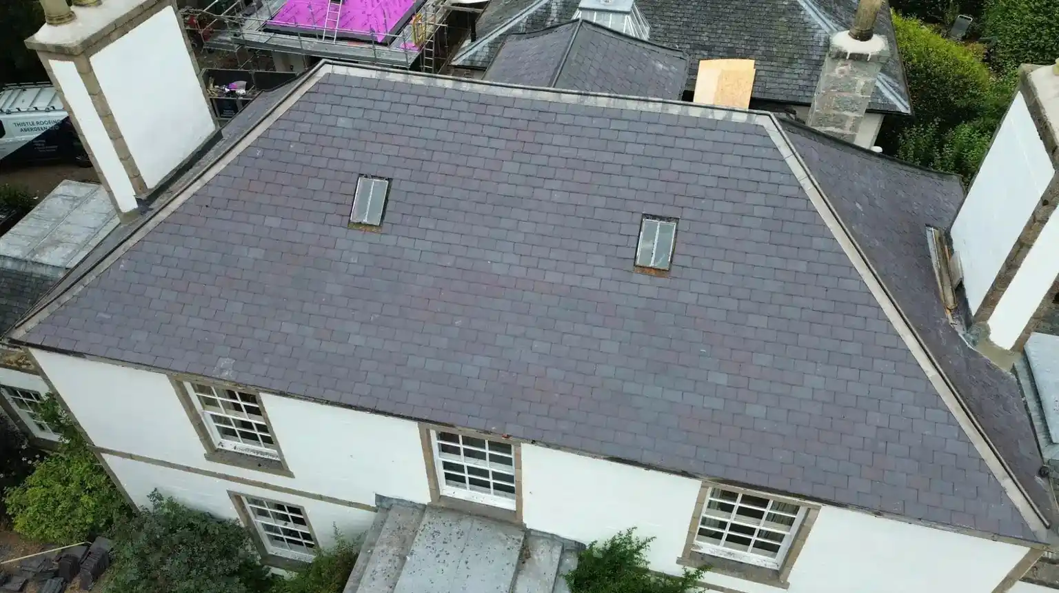 A slate roof seen from the air, with white walls and sash windows below