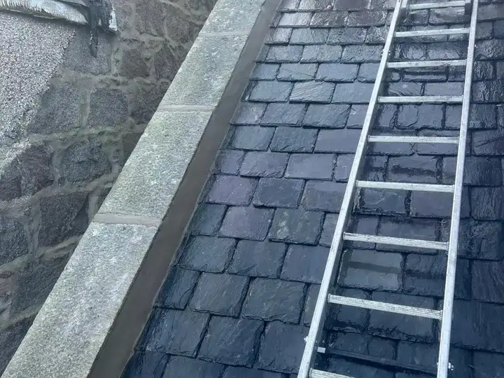 A roof ladder on a slate roof beside a granite skew