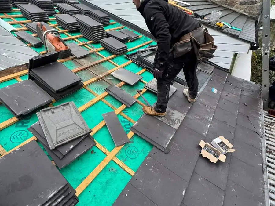 Roofer fixing new slates from a stack loaded out on the battens