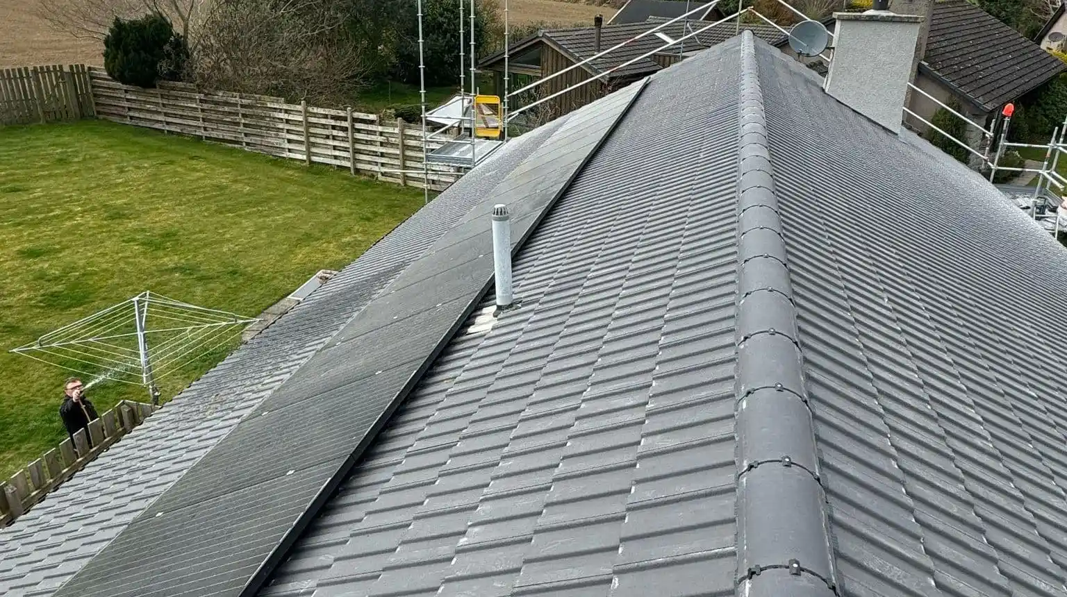 A new grey tiled roof with a dry-fixed ridge running the length of a bungalow, fields beyond